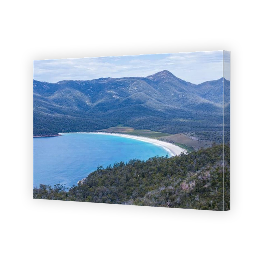 An aerial view of a horseshoe-shaped stretch of white sand surrounded by mountains.