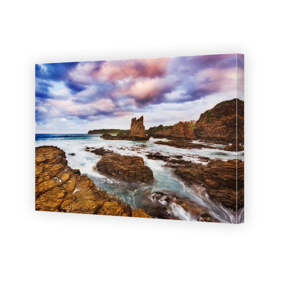 Rugged rocky coast around bombo beach in Kiama town on Australian Pacific shore. Blurred surf flows ashore eroding sandstone cliffs and cathedral boul