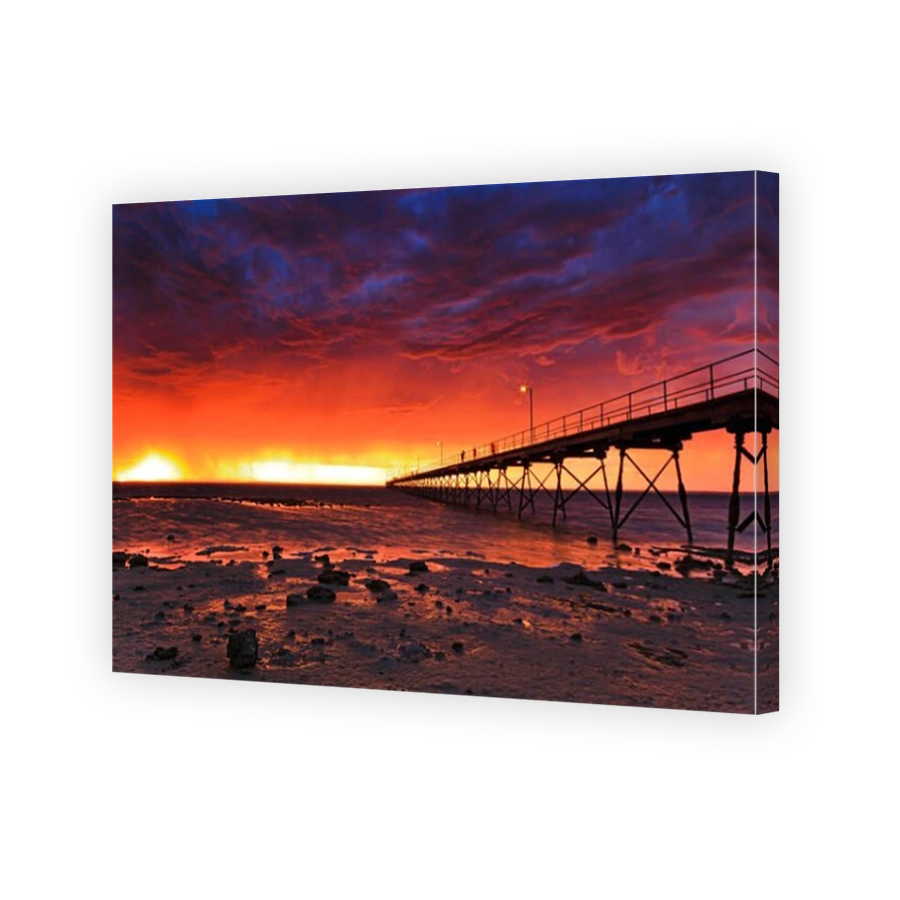 REd stormy sunset over horizon at Ceduna bay on Great Australian Bight. Historic timber jetty going towards open water at  tide