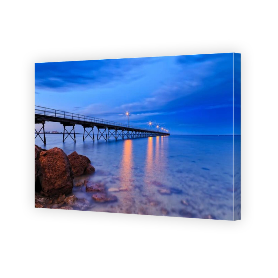 low point view of long wooden jetty and coastal rocks in Ceduna town bay when transparent water shows shallow seabed at sunrise.