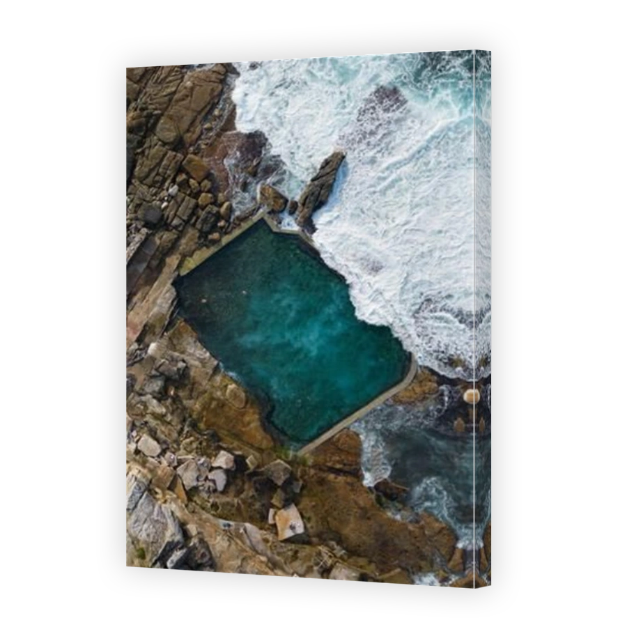 An aerial view of a serene and tranquil swimming pool in an ocean bay surrounded by large rocky cliffs: Mahon Pool, Maroubra, Sydney, Australia