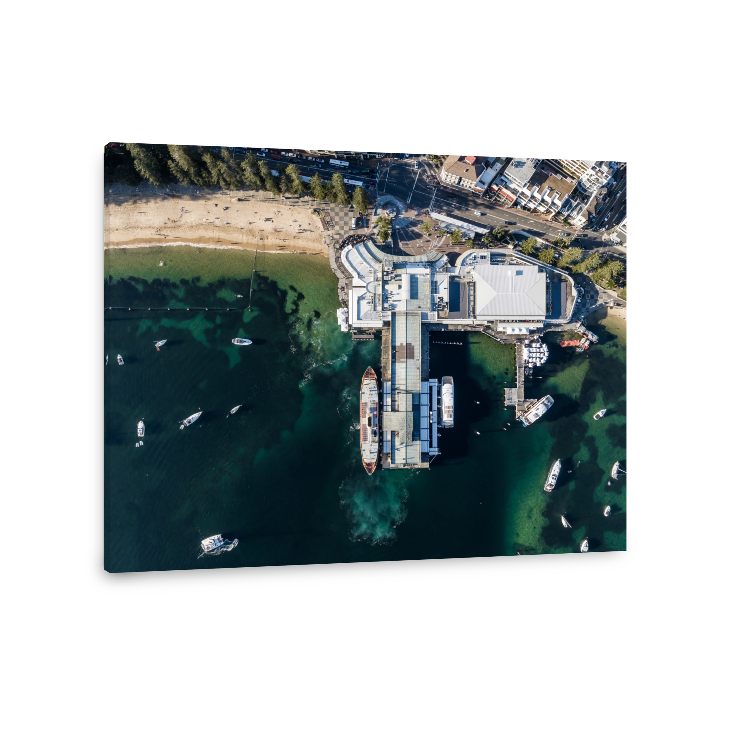 Vertical bird's eye aerial evening drone view of Manly wharf, part of the oceanside suburb of Manly, Sydney, New South Wales, Australia. Three ferries docked at the wharf. Manly Cove beach to the left