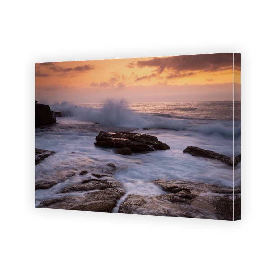 Coastal sunrise waves crashing onto rocks in golden orange light