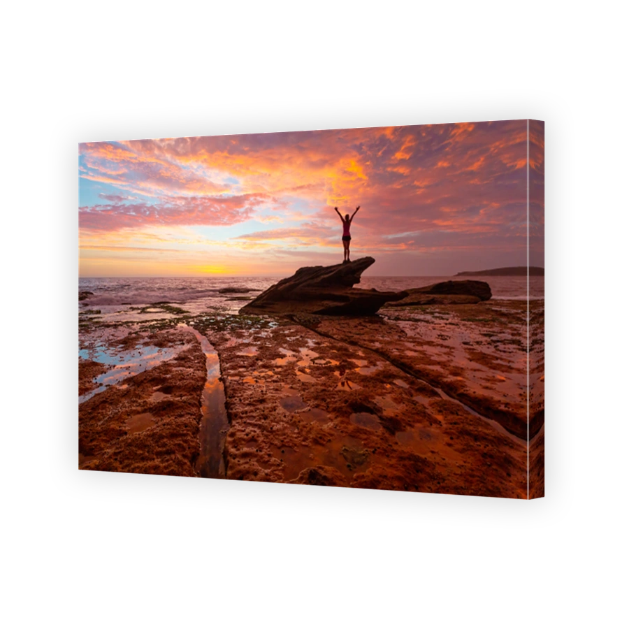 Female standing on large coastal jagged rock viewing red sunrise skies