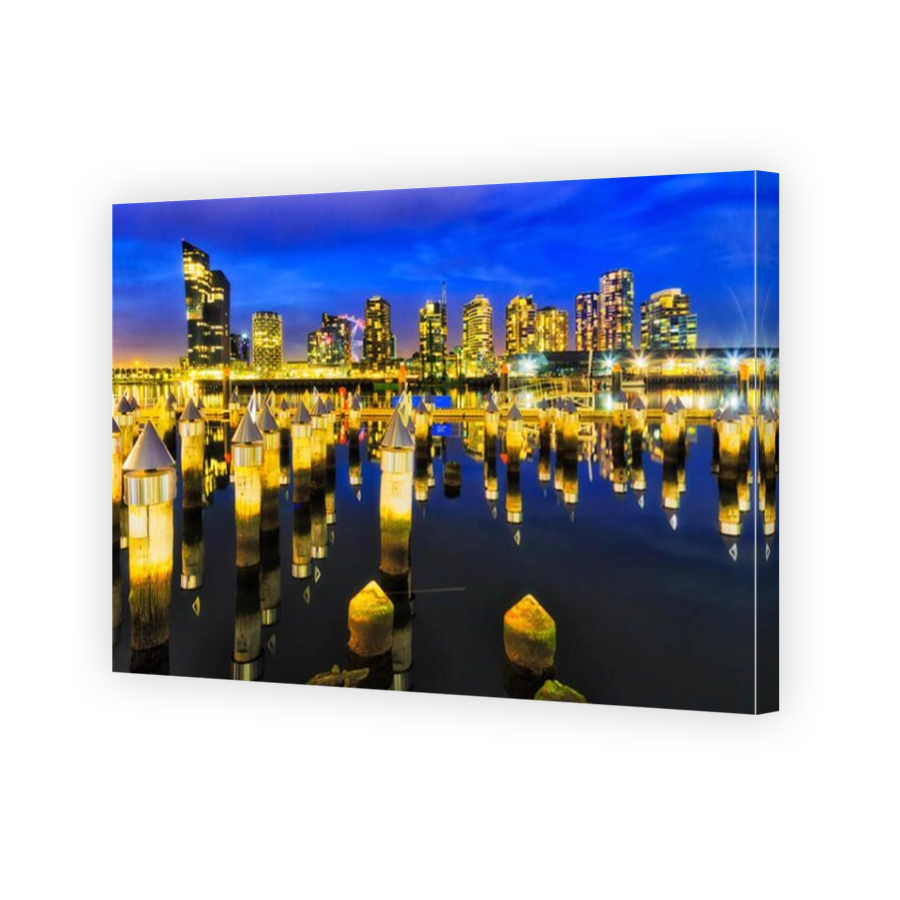Matrix of timber jetty poles pinning out of still waters of Yarra river at Melbourne's docklands marina and suburb at sunset with bright reflecting il