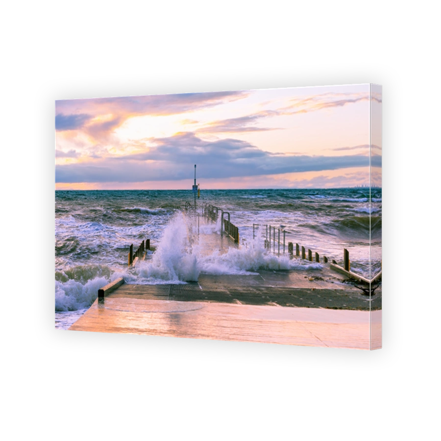 Large wave splashes protruding through boat jetty on ocean coastline at sunset