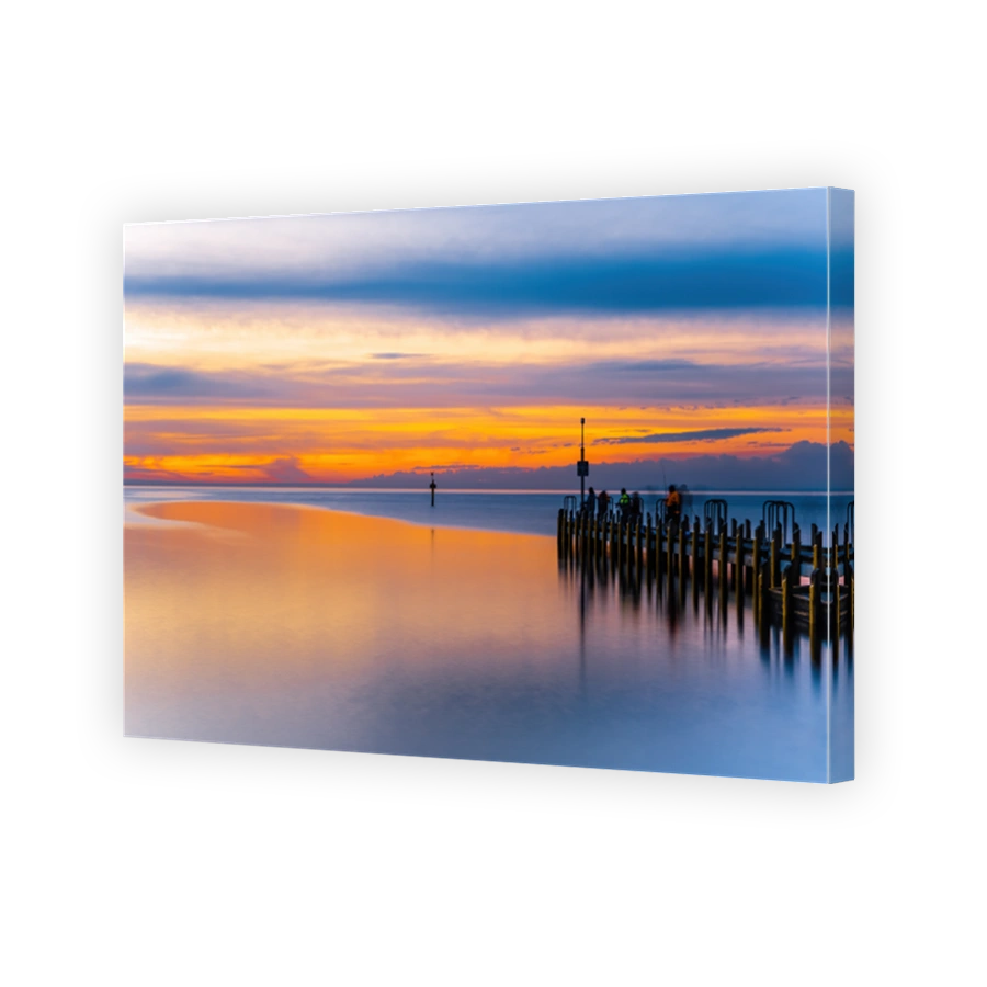 Vivid glowing orange sunset over ocean and boat jetty - long exposure seascape