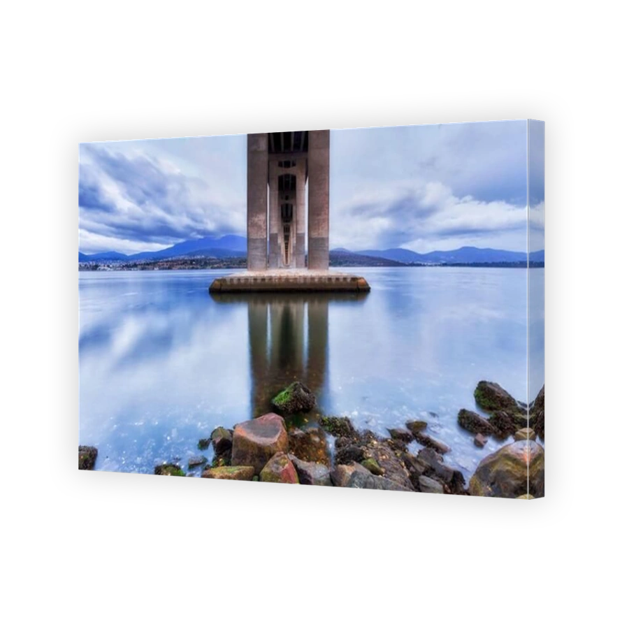 Underneath the Tasman bridge across Derwent river in Hobart at sunrise when clouds and lights reflect in still waters.
