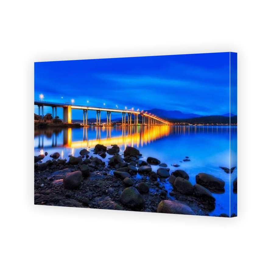 Tasman bridge across Derwent river at sunrise during blue hour with bright illumination lights in view of Hobart city waterfront.