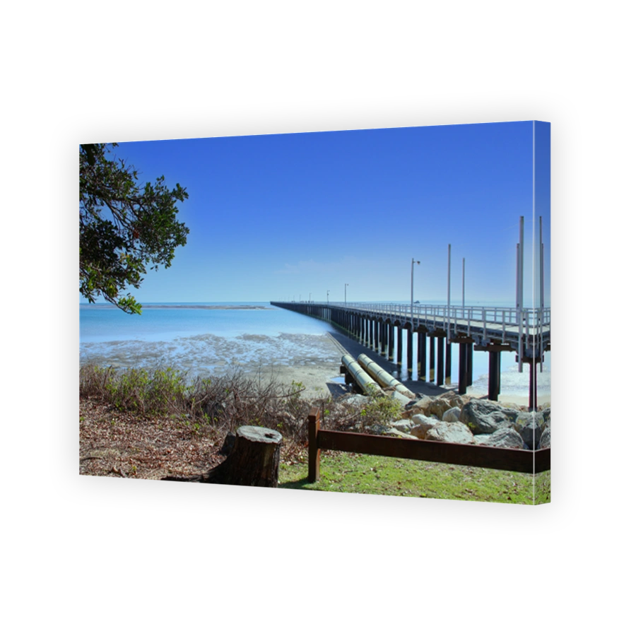 Looking out to the Urangan Pier in Urangan.  Green grass and trees.  Blue water in the bay.  Blue skies.  Hervey Bay Queensland Australia