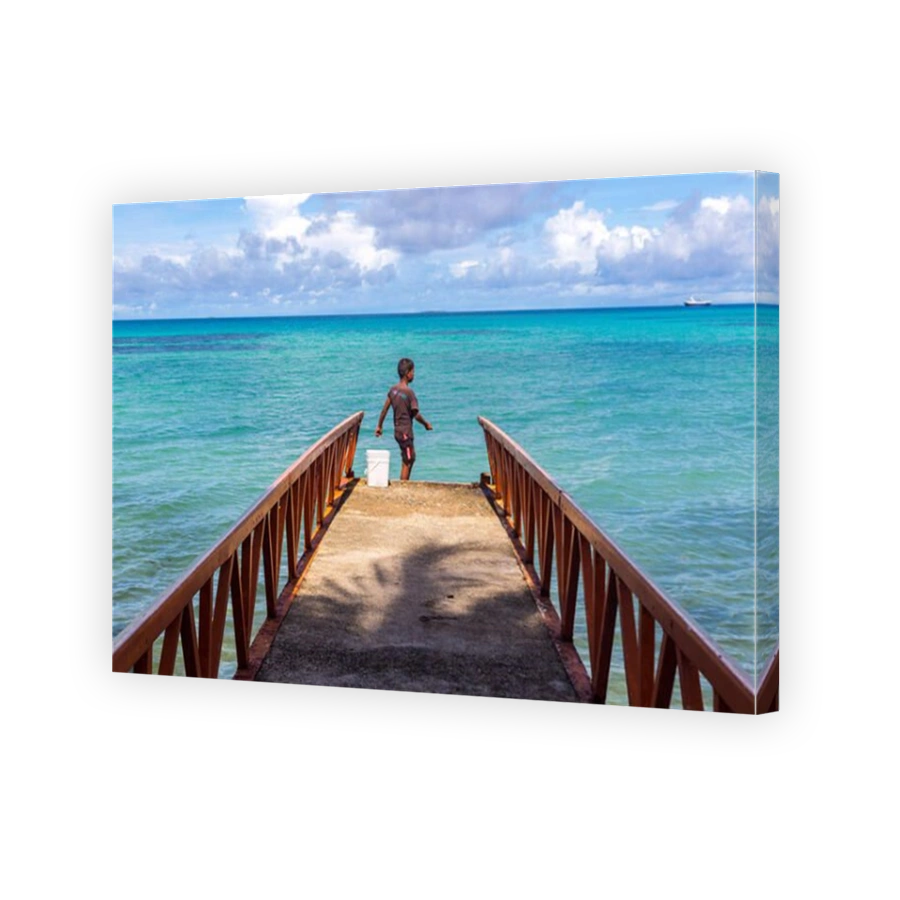 A local Polynesian boy fishing from a jetty pier in a tropical azure turquoise blue lagoon in Vaiaku, Funafuti atoll, Tuvalu, Polynesia, Oceania.
