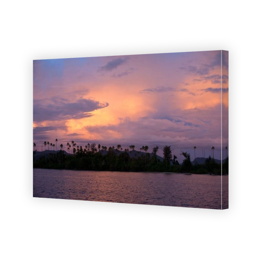 Early morning light reflects off clouds hanging over a low lying island amid the Solomon Archipelago.