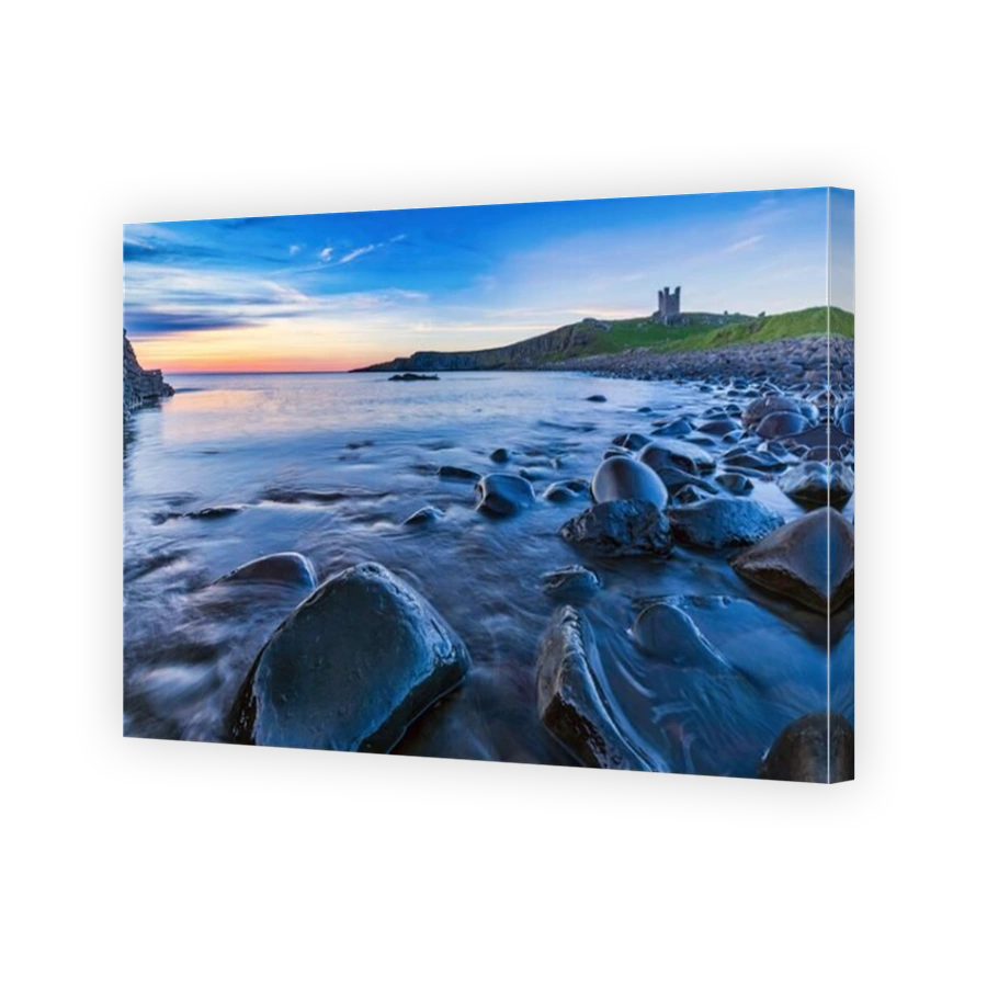 Dunstanburgh Castle at sunrise from Embleton Bay on the Northumberland coast, England, Uk