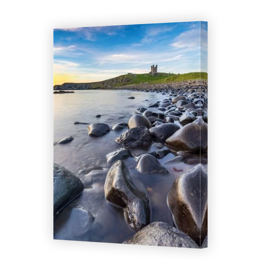 Dunstanburgh Castle at sunrise from Embleton Bay on the Northumberland coast, England, Uk