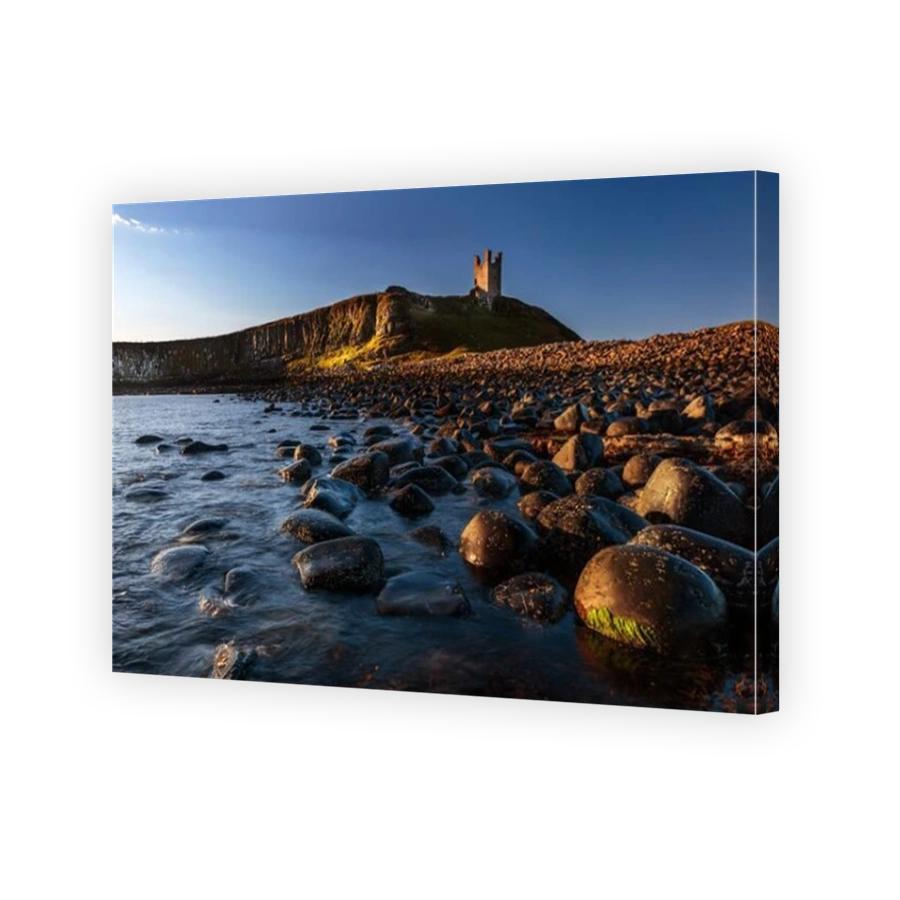 The ruins of Dunstanburgh Castle overlooking the boulder strewn shores of Embleton Bay, Northumberland, England