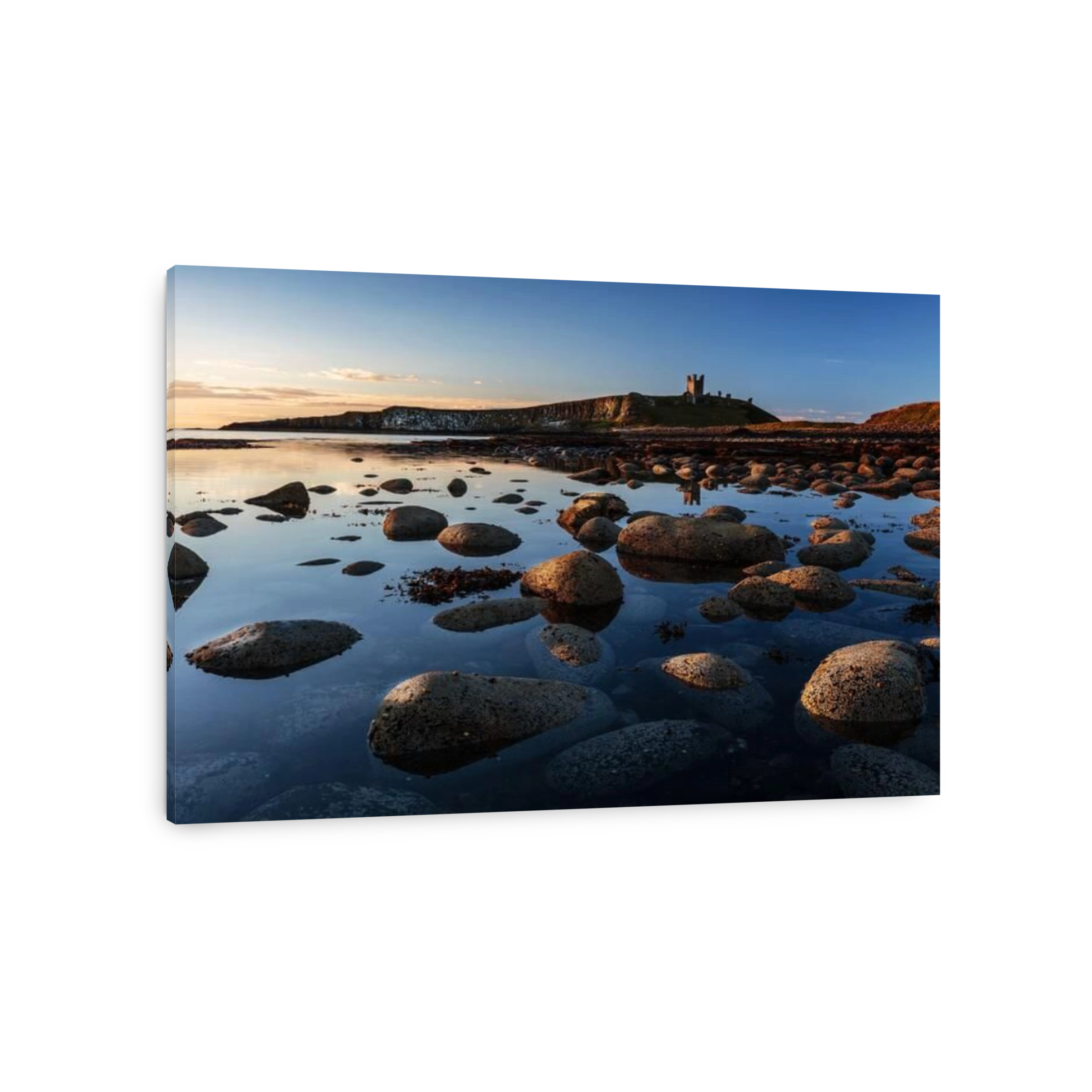 The ruins of Dunstanburgh Castle overlooking the boulder strewn shores of Embleton Bay, Northumberland, England