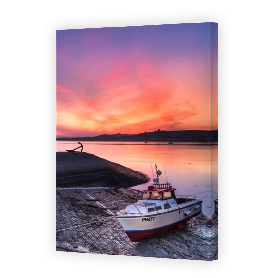 The sky turns pink over the River Torridge, as the sun rises at dawn behind Instow, lighting up a boat moored on the quay at Appledore in North Devon.