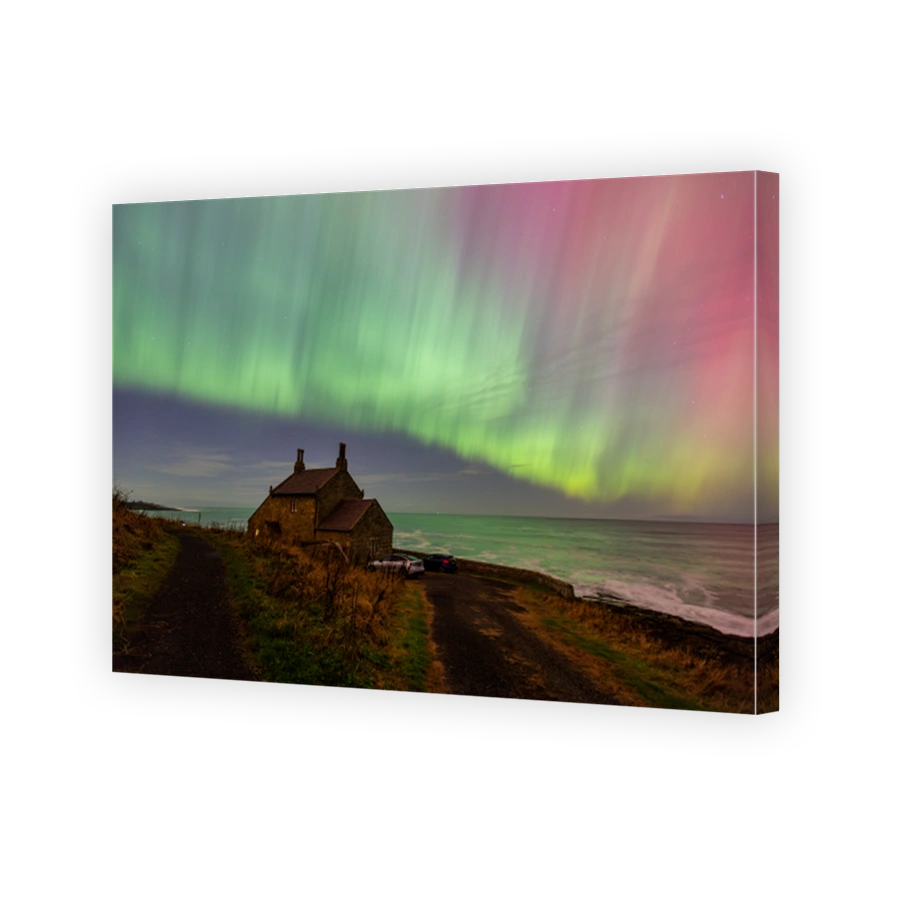 The Northern Lights over a cottage perched on cliffs overlooking the sea on the Northumberland coast during the extreme solar storm of 10th October 2024