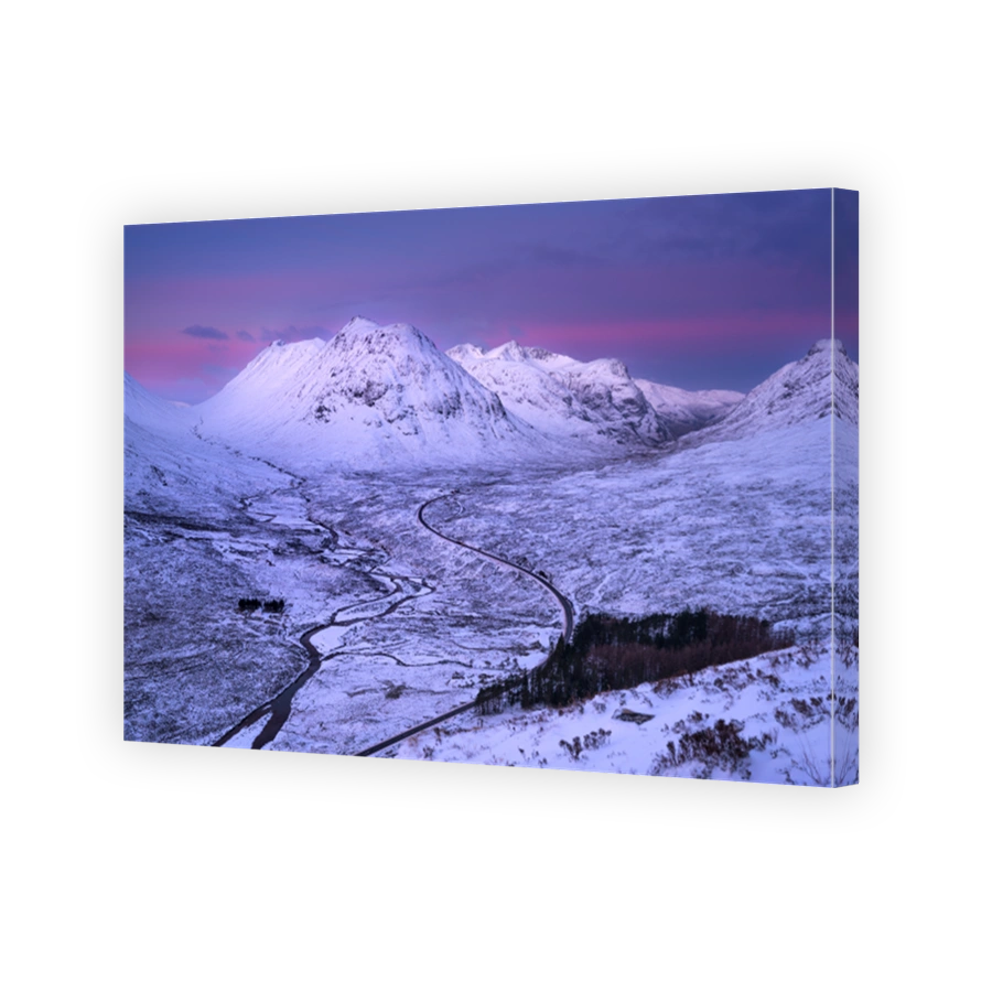 Long winding road leading through snow covered valley of Glencoe in the Scottish Highlands, UK.