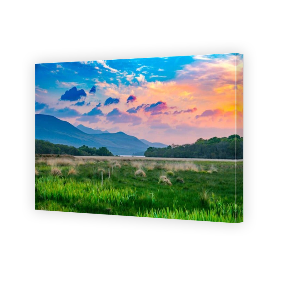 Vibrant and colorful mountain range sunset meadow with green grass and orange clouds