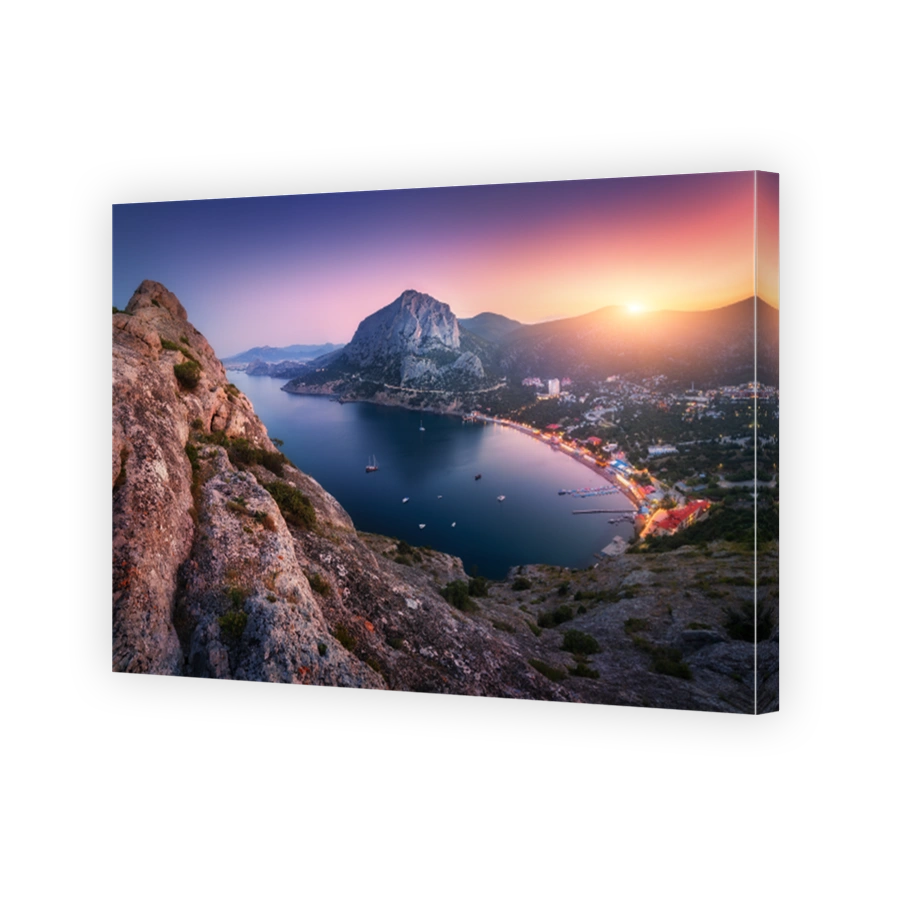 View from the mountain peak on the city, blue sea and high rocks against beautiful sky at sunset. Colorful mountain landscape in the evening. Vacation on seashore. Summer travel in Europe. City lights