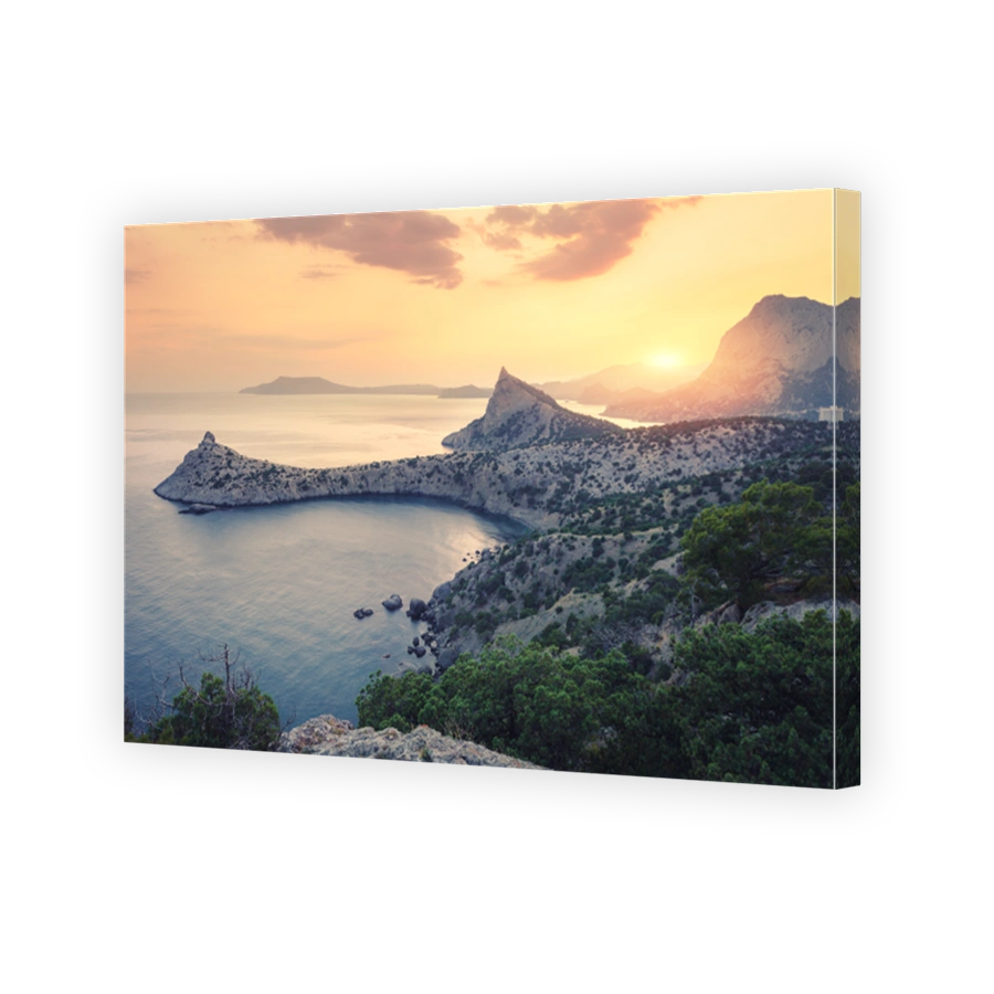 Beautiful sunrise in mountains at the sea. Amazing summer landscape with rocks, mountain forest, colorful bright orange sky with sun, blue water in the morning. Seascape at dawn. Nature background
