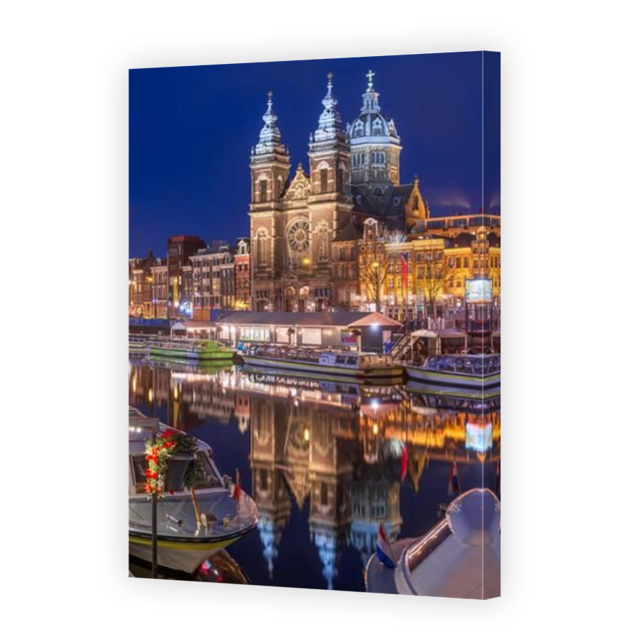 Amsterdam, Netherlands city center view with riverboats and the  Basilica of Saint Nicholas at night.