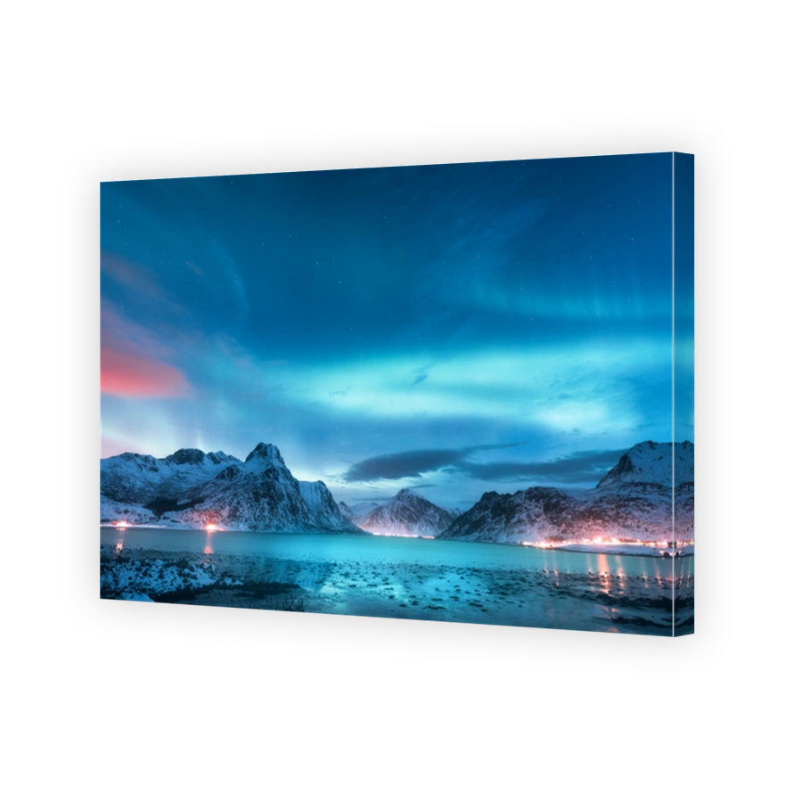 Aurora borealis over the sea coast, snowy mountains and city lights at night. Northern lights in Lofoten islands, Norway. Starry sky with polar lights. Winter landscape with aurora reflected in water