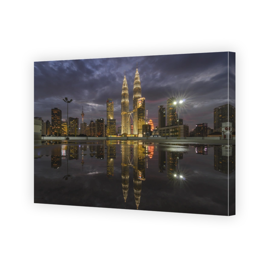 Reflection Of Illuminated Petronas Towers In River Amidst Buildings Against Cloudy Sky At Dusk