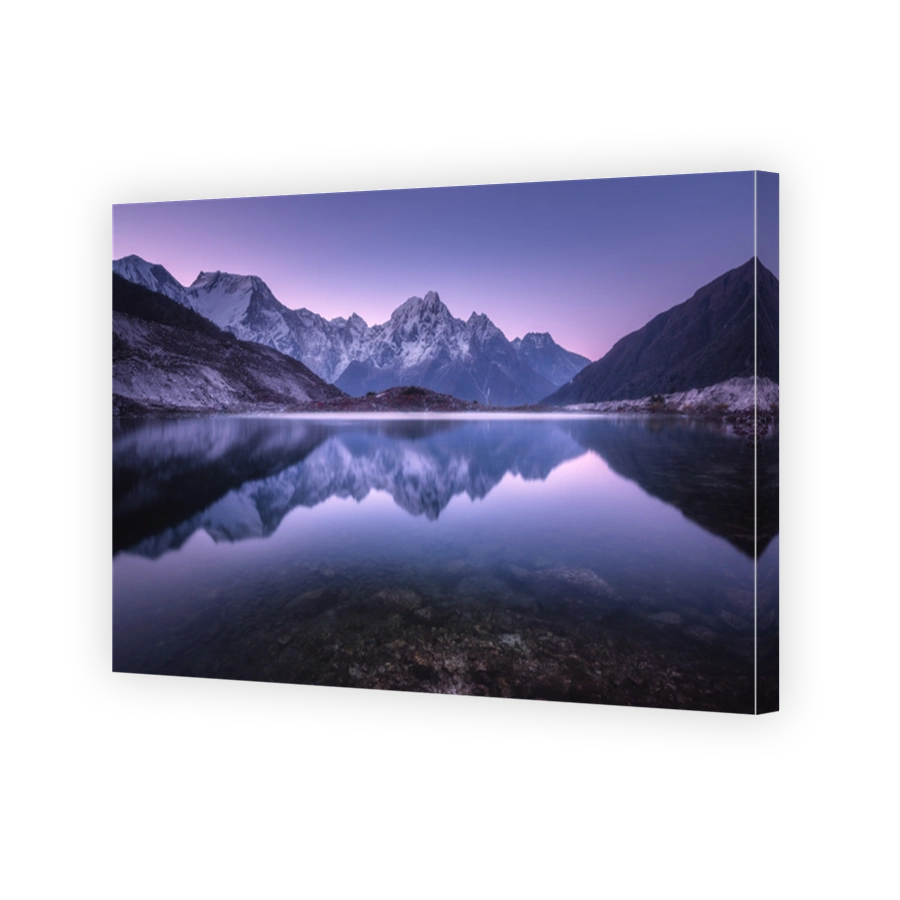 Mountain lake with perfect reflection at sunrise. Beautiful landscape with purple sky, snowy mountains, hills, fog over the lake at twilight in Nepal. Snow covered rocks is reflected in water. Nature