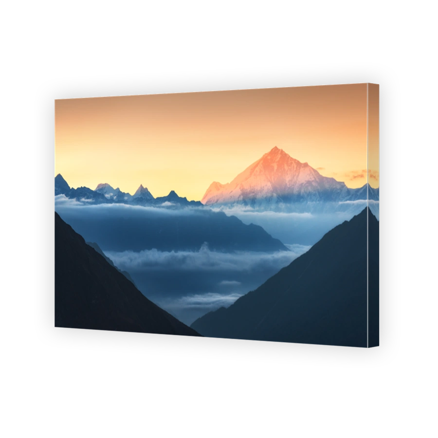 Majestic view of silhouettes of mountains and low clouds at colorful sunrise in Nepal. Landscape with snowy peaks of Himalayan mountains, beautiful sky and yellow sun rays. Amazing Himalayas. Nature