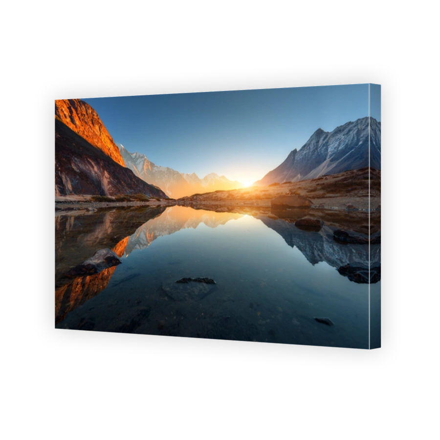 Wonderful landscape with high rocks with illuminated peaks, stones in mountain lake, reflection, blue sky and yellow sunlight in sunrise. Nepal. Amazing scene with Himalayan mountains. Himalayas