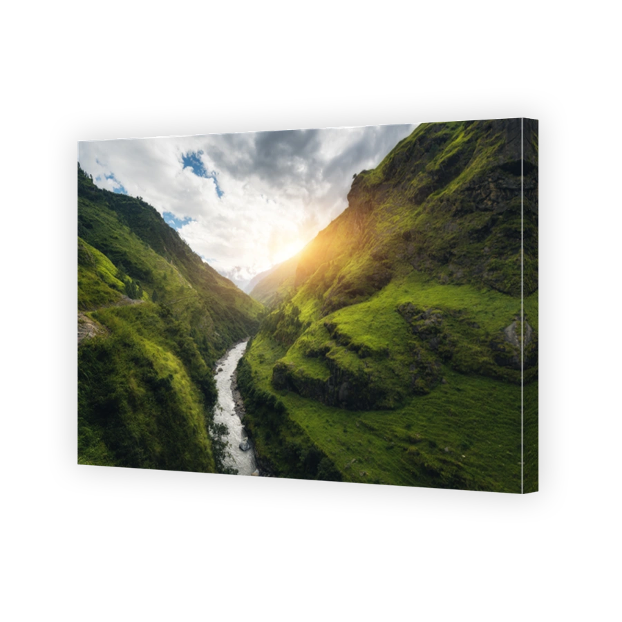 View with amazing Himalayan mountains covered green grass, river, meadows and forest, blue sky with clouds, sun and stones in water in autumn in Nepal at sunrise. Mountain valley. Travel in Himalayas
