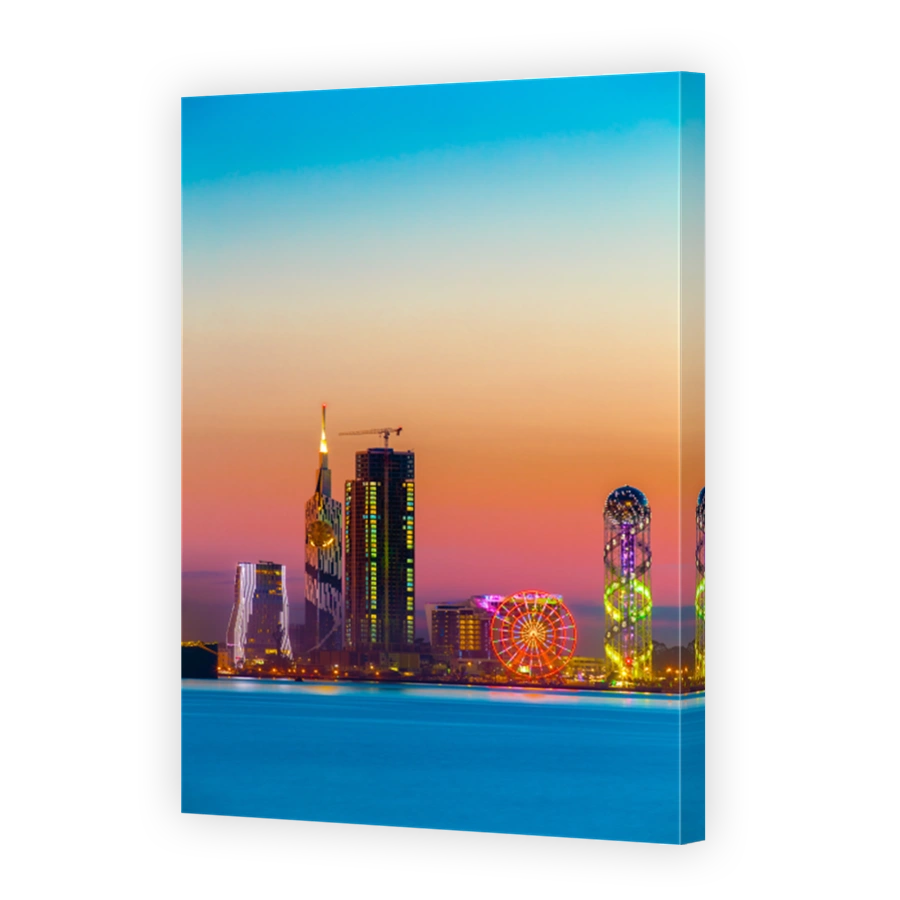 Batumi, Adjara, Georgia. Sunset Or Sunrise. Bright Evening Sky In Yellow, Orange And Purple Colors. View From Sea Beach To Illuminated Cityscape With Modern Urban Architecture, Skyscrapers And Tower.