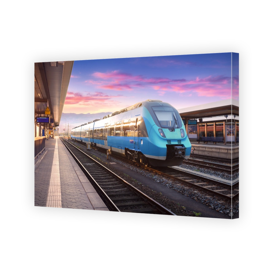 Beautiful view with modern commuter train on the railway station and colorful sky with clouds at sunset in Europe. Industrial landscape with blue train on railway platform. Railroad background