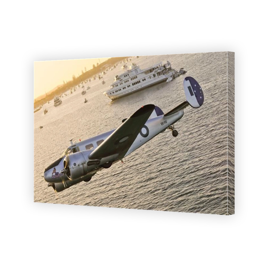 An air to air shot of a restored RAAF twin engine, Beech 18 Expeditor aircraft flying low over the sea near a tour ship.