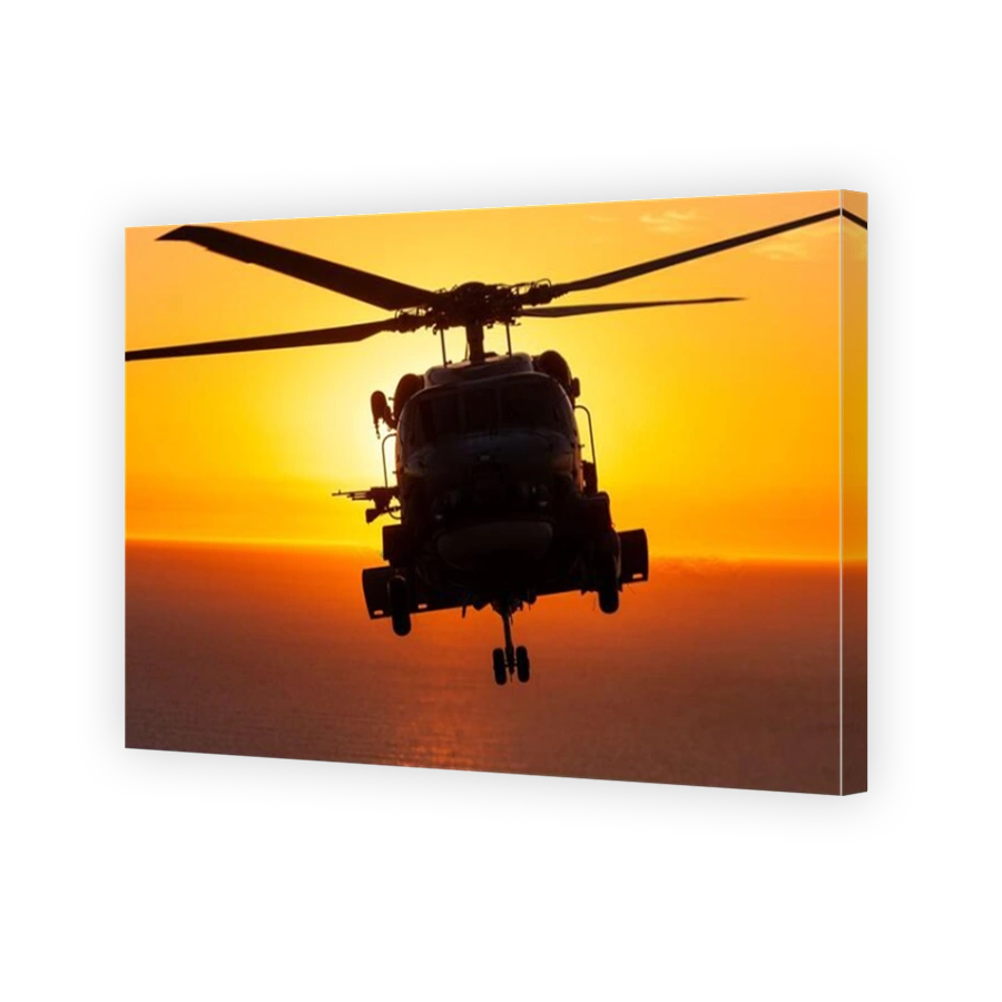 An air-to-air view of a Naval Sikorsky S70B Seahawk helicopter in silhouette, at sunset.