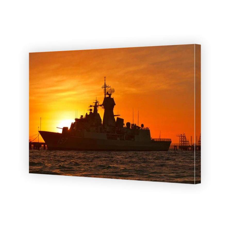 A silhouette of an Australian Navy Frigate at sunrise, tied up alongside a small jetty.